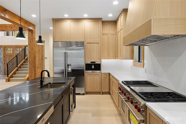 kitchen featuring custom exhaust hood, high end appliances, sink, dark stone countertops, and hanging light fixtures