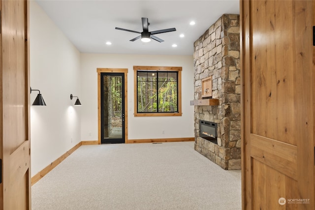 living room with carpet flooring, a stone fireplace, ceiling fan, and heating unit