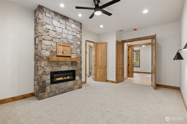 carpeted living room with a stone fireplace and ceiling fan