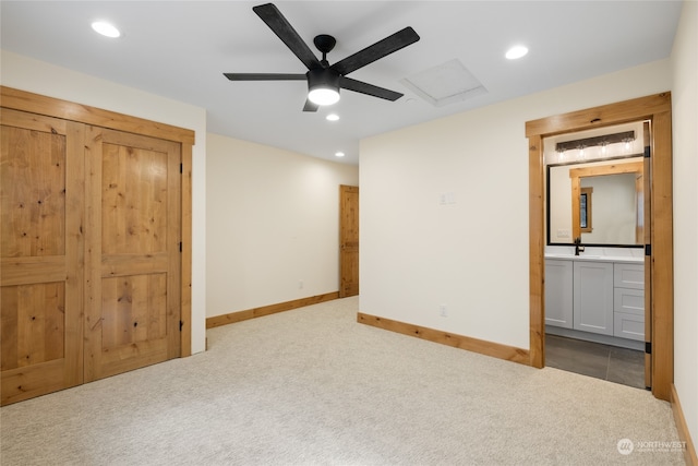 unfurnished bedroom featuring ceiling fan, light colored carpet, sink, and ensuite bath