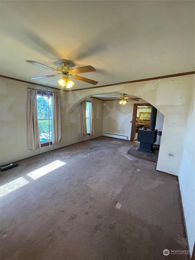 unfurnished living room featuring dark carpet, a wood stove, ceiling fan, and a baseboard heating unit