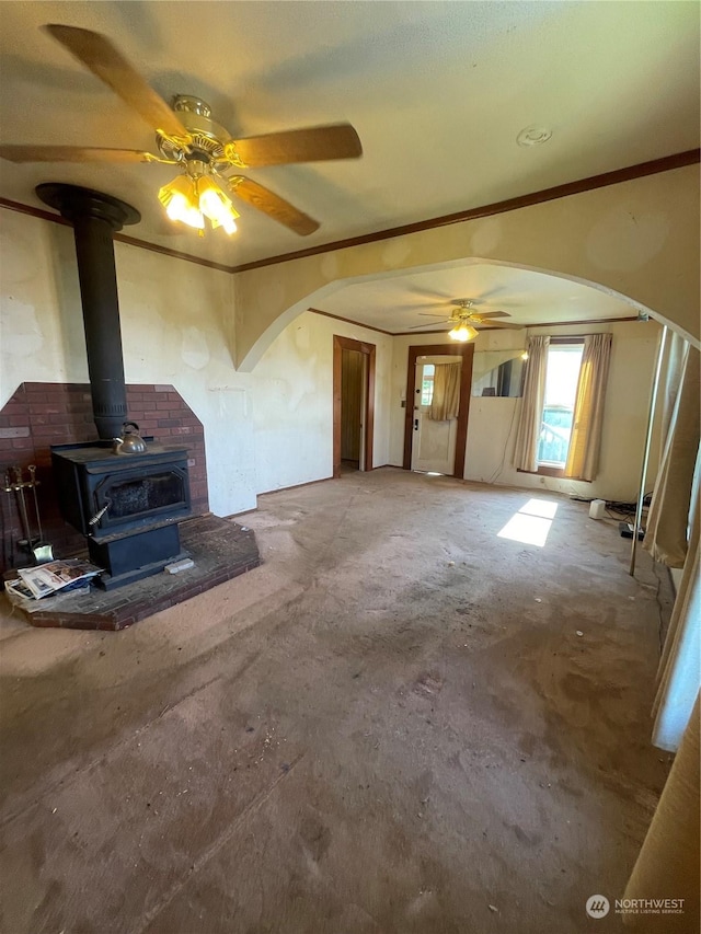 unfurnished living room featuring a wood stove, ceiling fan, carpet, and ornamental molding