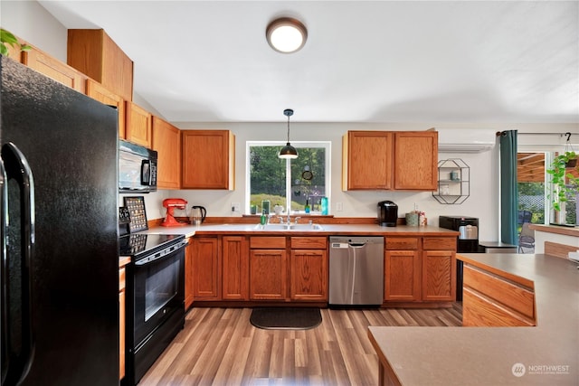 kitchen featuring black appliances, an AC wall unit, sink, hanging light fixtures, and light wood-type flooring