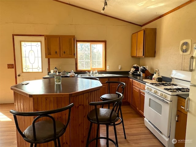 kitchen with light hardwood / wood-style floors, gas range gas stove, vaulted ceiling, a kitchen island, and sink