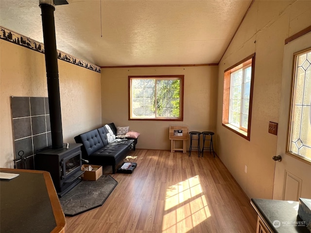 sitting room with vaulted ceiling, hardwood / wood-style flooring, a wood stove, and a textured ceiling