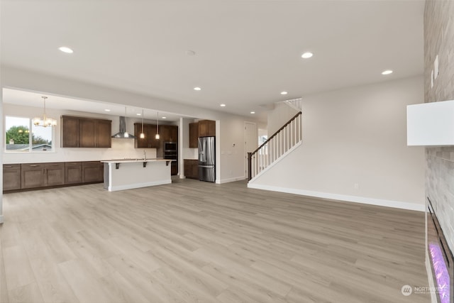 unfurnished living room featuring a stone fireplace, an inviting chandelier, and light wood-type flooring