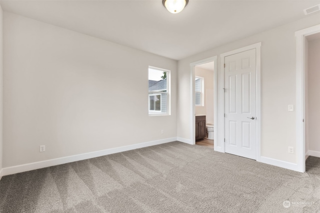 unfurnished bedroom featuring a closet, ensuite bathroom, and carpet flooring