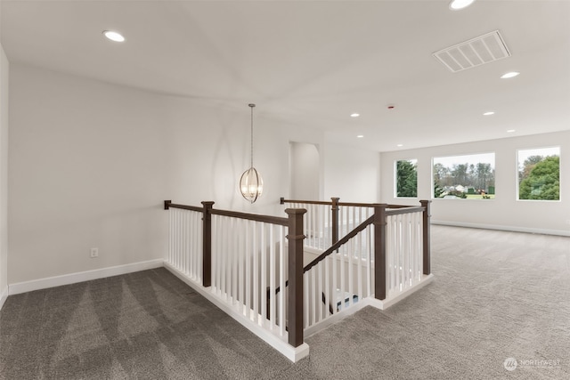 hallway featuring dark carpet and an inviting chandelier