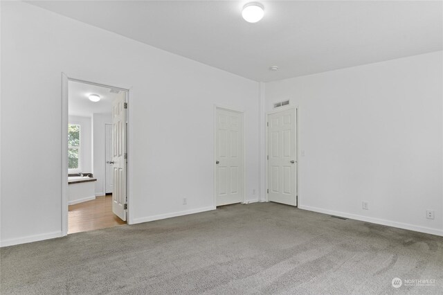 unfurnished bedroom with ensuite bath, lofted ceiling, and carpet