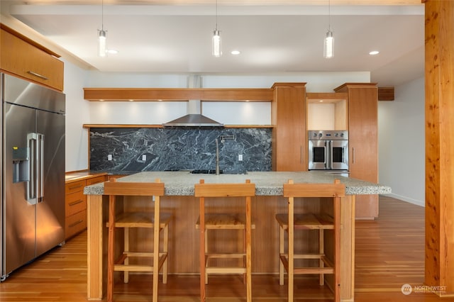 kitchen featuring hanging light fixtures, wall chimney exhaust hood, stainless steel appliances, and light hardwood / wood-style floors