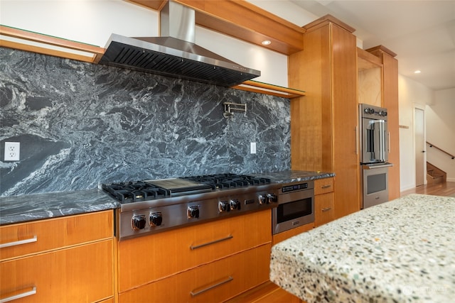 kitchen with stainless steel appliances, tasteful backsplash, hardwood / wood-style floors, wall chimney exhaust hood, and dark stone countertops