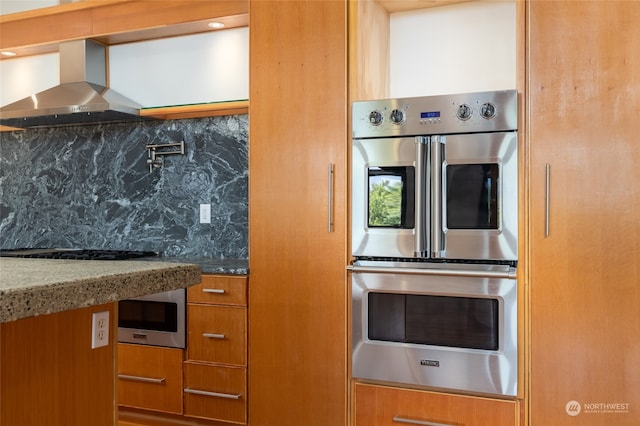 kitchen with stainless steel appliances, light stone countertops, wall chimney exhaust hood, and tasteful backsplash