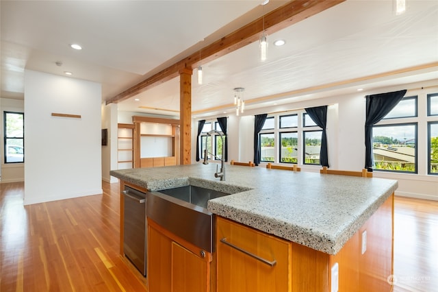 kitchen featuring light stone counters, hanging light fixtures, a center island with sink, light wood-type flooring, and sink