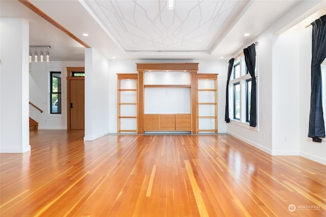 unfurnished living room featuring a raised ceiling and light wood-type flooring