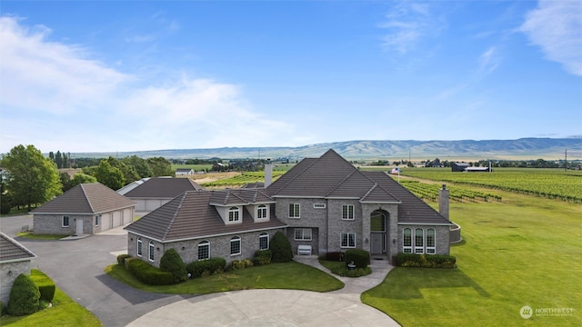 french country inspired facade featuring a front yard, a mountain view, and a garage