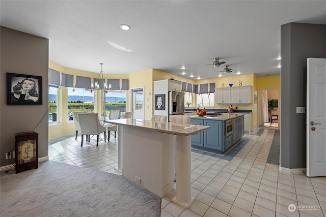 kitchen with blue cabinets, a kitchen island, stainless steel fridge with ice dispenser, white cabinetry, and ceiling fan with notable chandelier