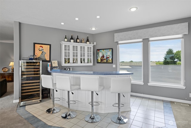 bar featuring a water view, beverage cooler, white cabinetry, and light colored carpet