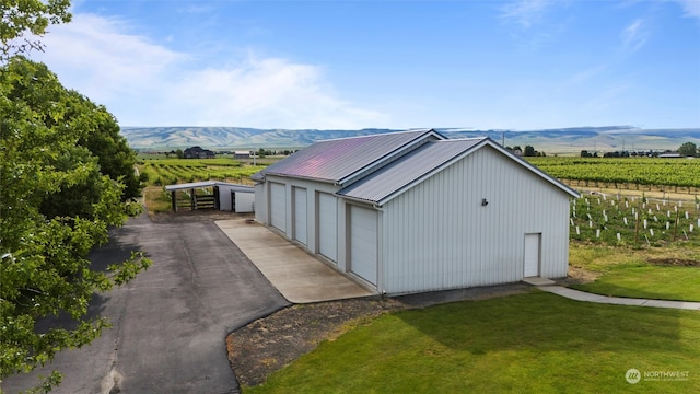 view of property exterior with a mountain view, a garage, a rural view, and an outbuilding