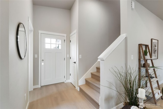 foyer entrance featuring stairs, light wood finished floors, and baseboards