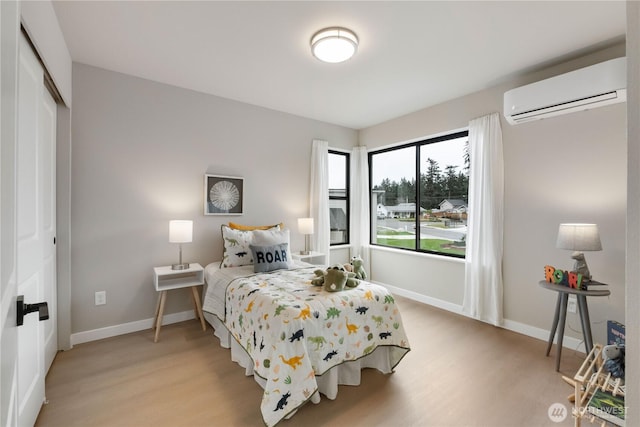 bedroom with light wood finished floors, a wall mounted AC, a closet, and baseboards