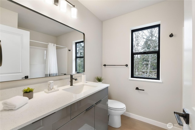 bathroom featuring a healthy amount of sunlight, baseboards, toilet, and vanity