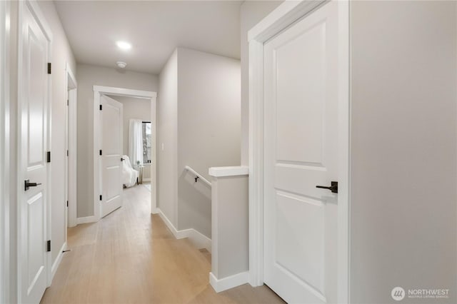 hall with light wood-type flooring, baseboards, and an upstairs landing