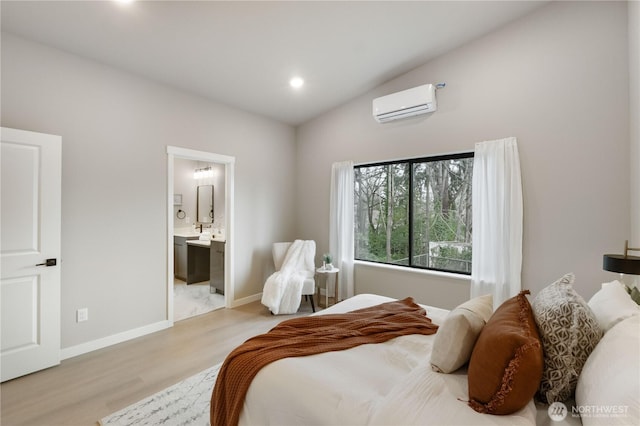 bedroom featuring baseboards, light wood-style flooring, ensuite bathroom, vaulted ceiling, and an AC wall unit