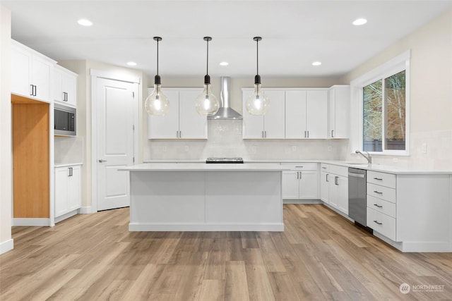 kitchen featuring wall chimney range hood, decorative light fixtures, white cabinets, light hardwood / wood-style floors, and a kitchen island