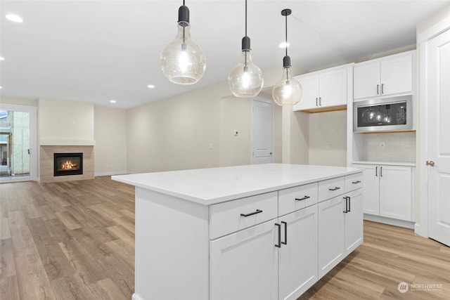 kitchen with hanging light fixtures, a tile fireplace, white cabinetry, and stainless steel microwave