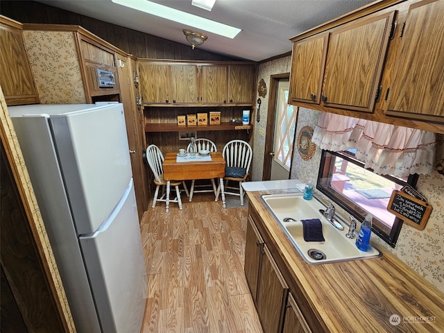 kitchen featuring light countertops, brown cabinetry, freestanding refrigerator, and wallpapered walls