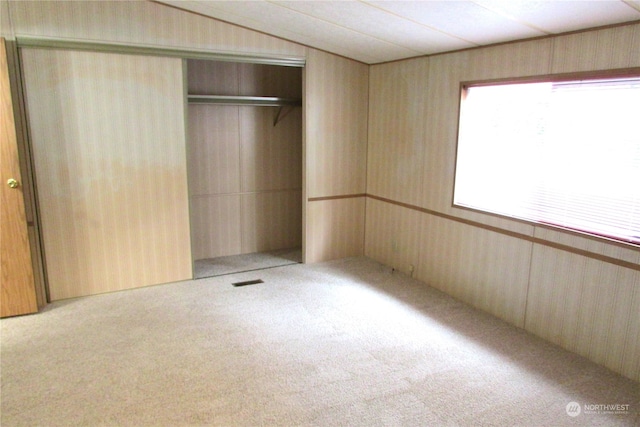 unfurnished bedroom with wooden walls, a closet, and light colored carpet