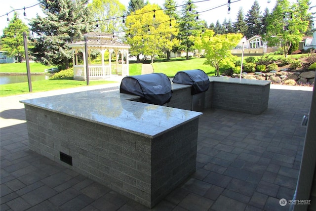 view of patio / terrace with a gazebo, a water view, grilling area, and exterior kitchen