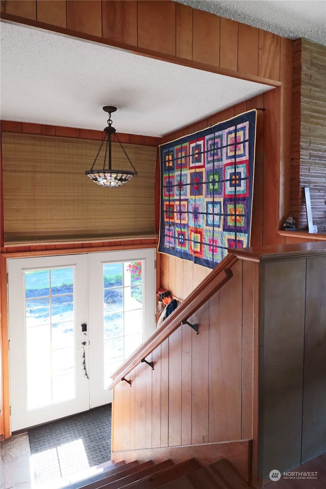 stairway featuring a textured ceiling, wooden walls, and french doors