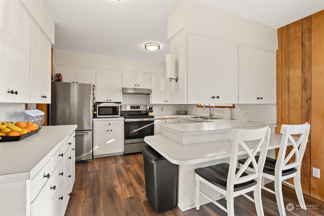 kitchen with dark wood-type flooring, white cabinets, a kitchen breakfast bar, sink, and appliances with stainless steel finishes