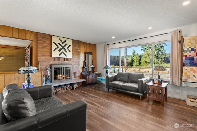 living room with a fireplace, wood-type flooring, a textured ceiling, and wooden walls