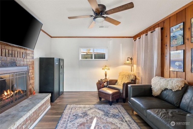 living room featuring a brick fireplace, ceiling fan, ornamental molding, a textured ceiling, and dark hardwood / wood-style flooring