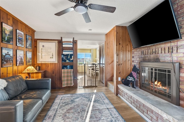 living room with a fireplace, wood-type flooring, ceiling fan, and wooden walls