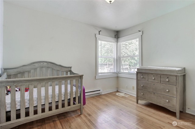 bedroom featuring a crib, light hardwood / wood-style flooring, and baseboard heating