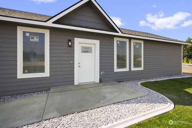 view of exterior entry with a patio, a yard, and a shingled roof