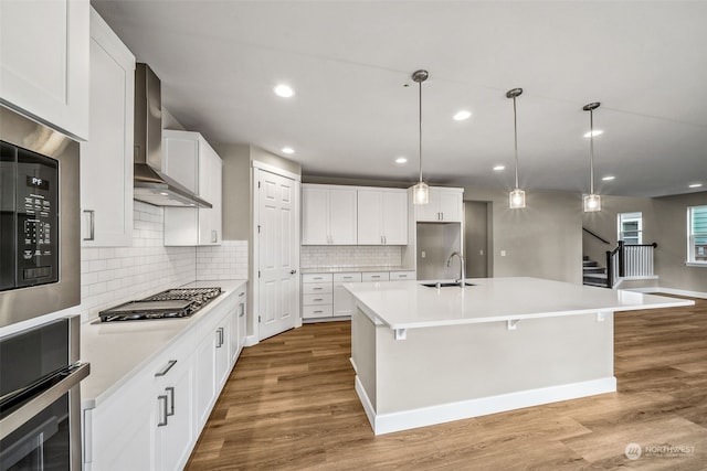 kitchen featuring white cabinetry, stainless steel appliances, wall chimney range hood, and light hardwood / wood-style flooring