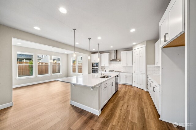 kitchen with wall chimney range hood, light hardwood / wood-style flooring, white cabinets, and sink