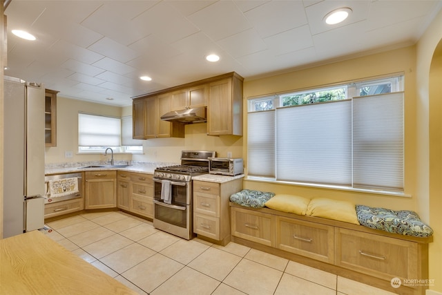 kitchen with white refrigerator, light brown cabinetry, double oven range, sink, and light tile floors