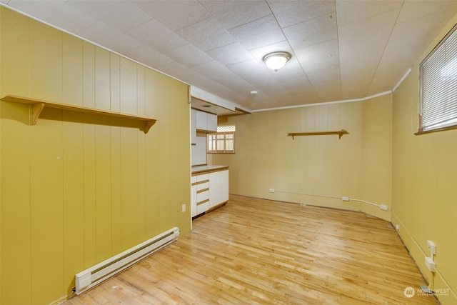 empty room with a wealth of natural light, baseboard heating, and light hardwood / wood-style flooring