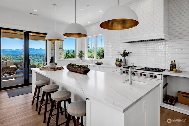 kitchen with a mountain view, pendant lighting, white cabinetry, and an island with sink