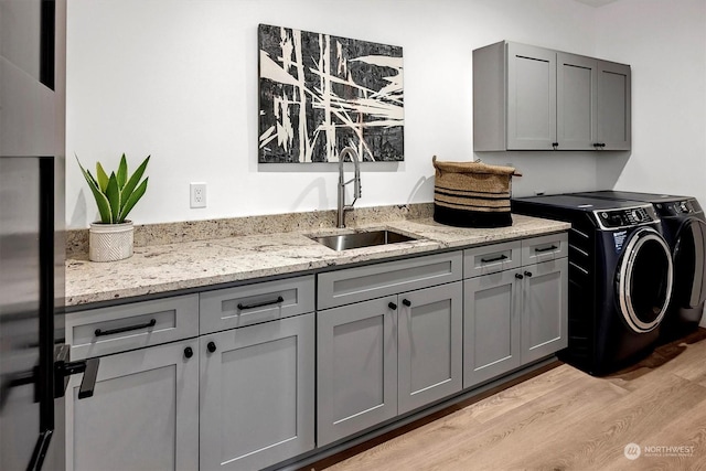 clothes washing area featuring sink, light hardwood / wood-style flooring, cabinets, and independent washer and dryer