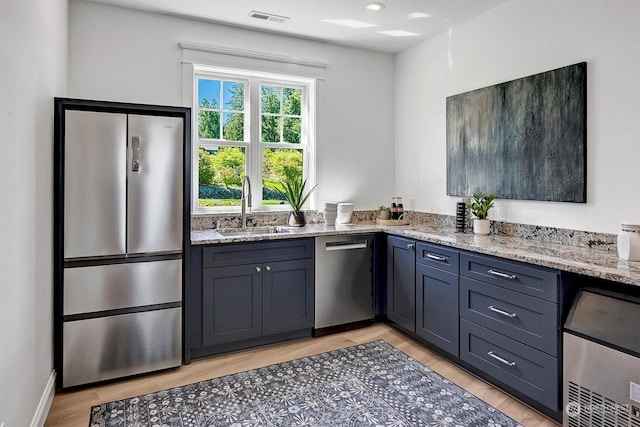 kitchen with light stone countertops, sink, light hardwood / wood-style flooring, and appliances with stainless steel finishes