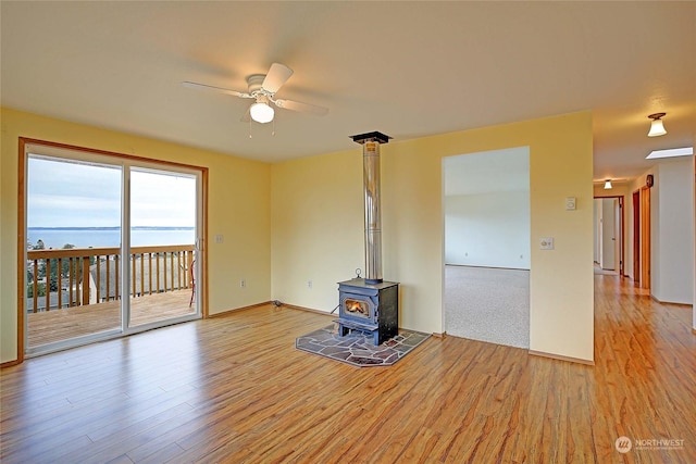 unfurnished living room with ceiling fan, a water view, a wood stove, and light hardwood / wood-style flooring