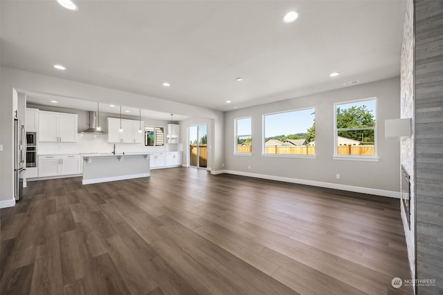 unfurnished living room featuring plenty of natural light, dark hardwood / wood-style flooring, and a stone fireplace