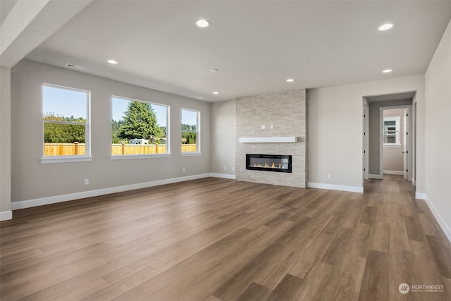 unfurnished living room with hardwood / wood-style flooring and a stone fireplace