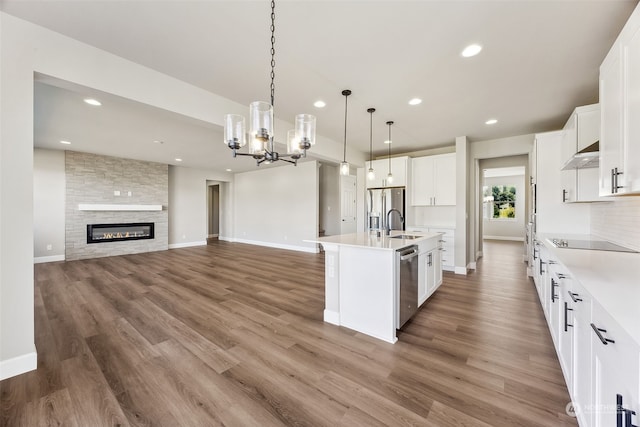 kitchen featuring a fireplace, an inviting chandelier, hardwood / wood-style floors, stainless steel appliances, and a kitchen island with sink